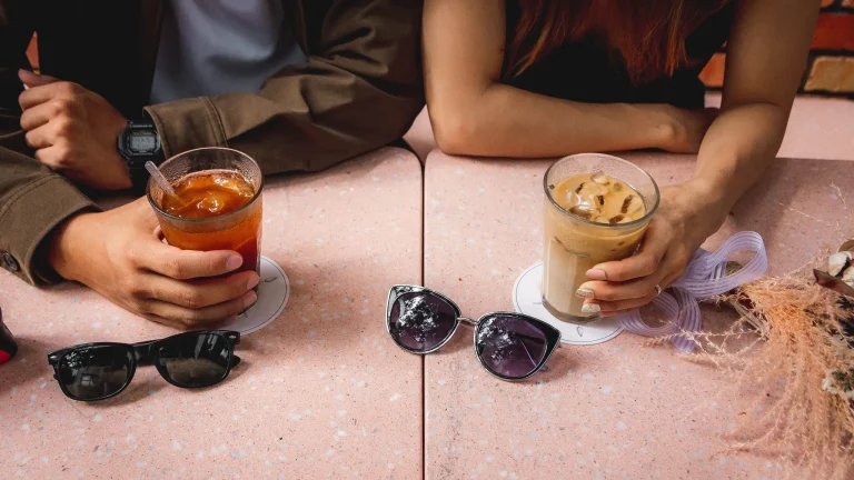 Two friends talking over drinks at an outdoor table, only their hands in view