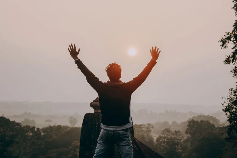 A man seen from behind with arms raised toward the sunrise, a picture of freedom