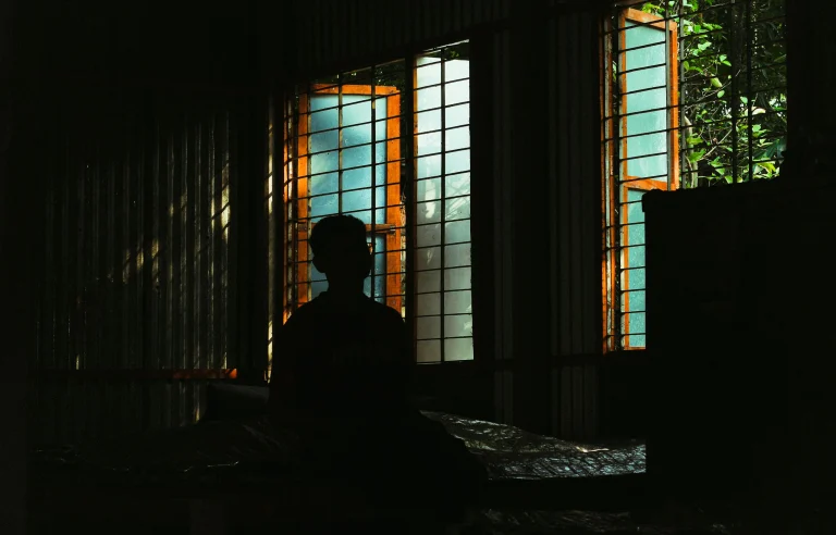 Silhouette of a person sitting by a bright window in a dark room