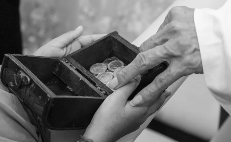 Black and white close-up of hands placing coins in a small wooden box
