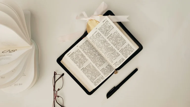 An open Bible with glasses, pen and calendar on a white table, ready for a step-by-step prayer session