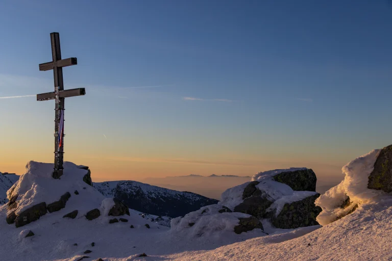 A cross on a snowy mountain top against the sunrise sky