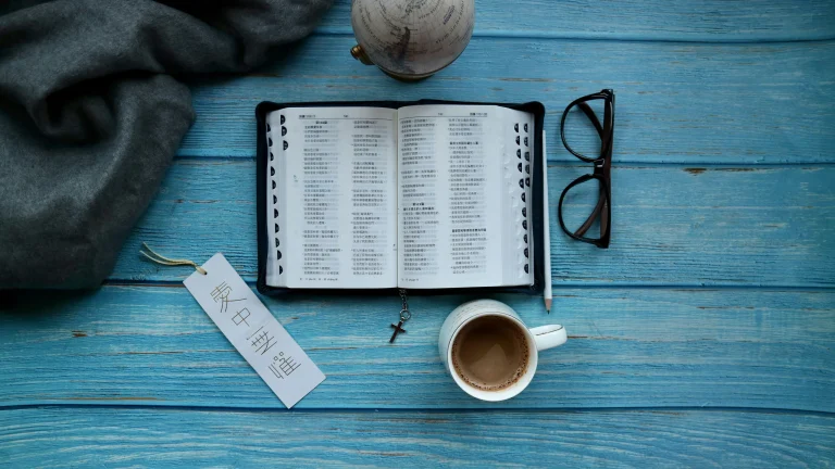 An open Bible with coffee and glasses on a blue wooden table for quiet time with God