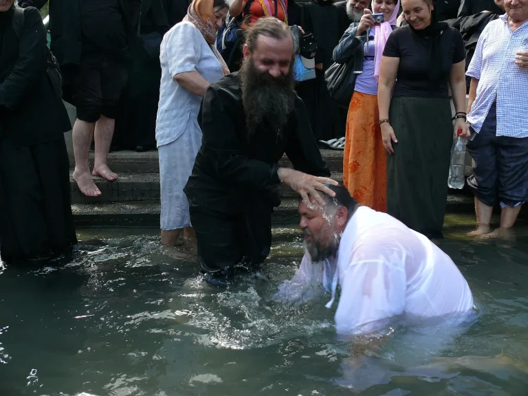 A believer being baptized by immersion in the Jordan River, with others standing in the water