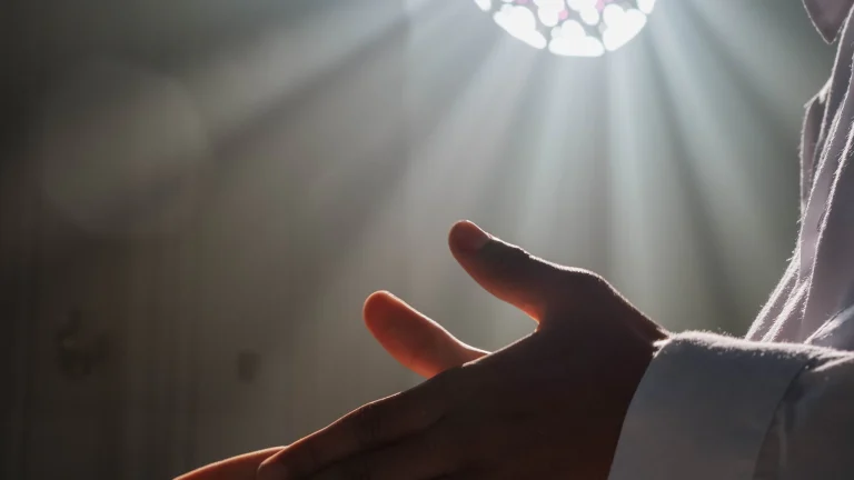 Open hands lifted in sunlight streaming through a church rose window